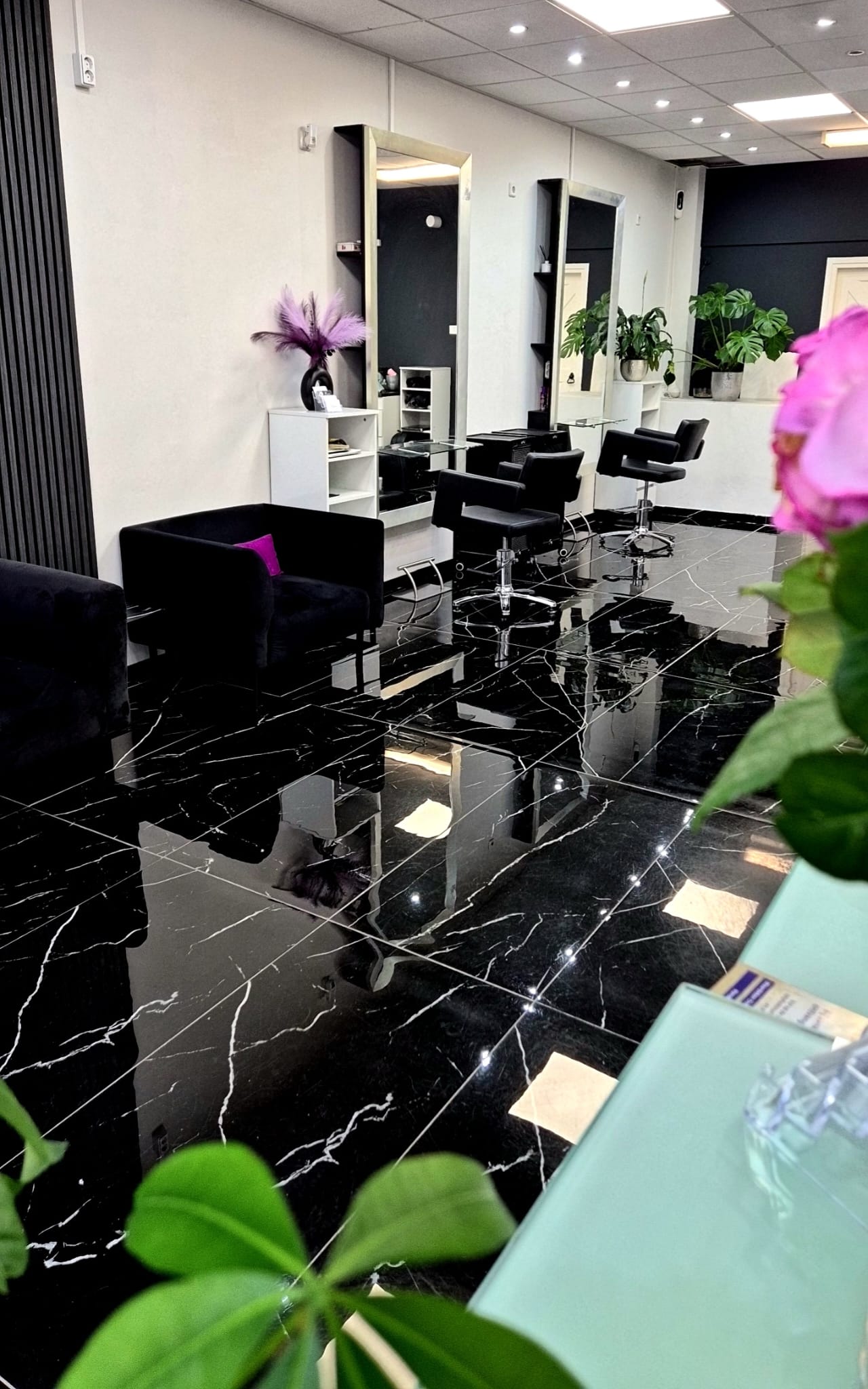 De salon: zwarte marmeren vloer, grote spiegels, zwarte stoelen en een paarse orchidee
